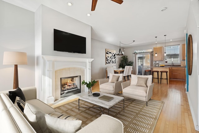 living room with a tiled fireplace, ceiling fan, light wood-type flooring, and recessed lighting