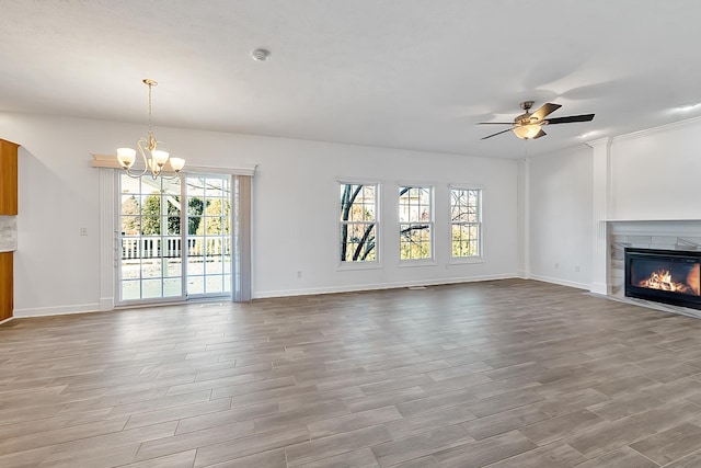 unfurnished living room with ceiling fan with notable chandelier, wood finished floors, a glass covered fireplace, and a wealth of natural light