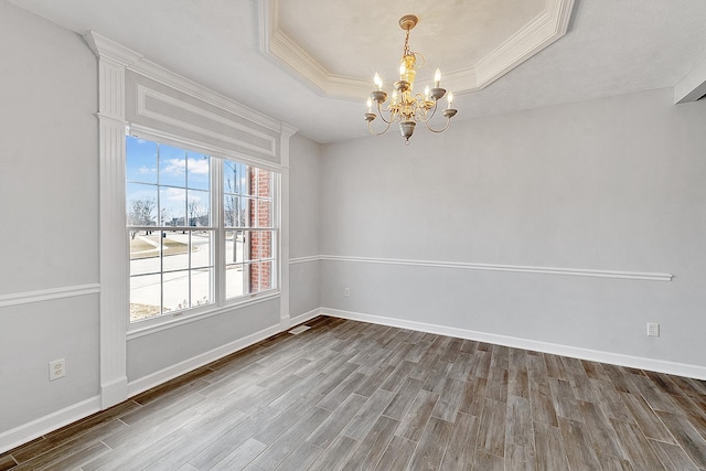 spare room featuring baseboards, wood finished floors, a tray ceiling, crown molding, and a notable chandelier