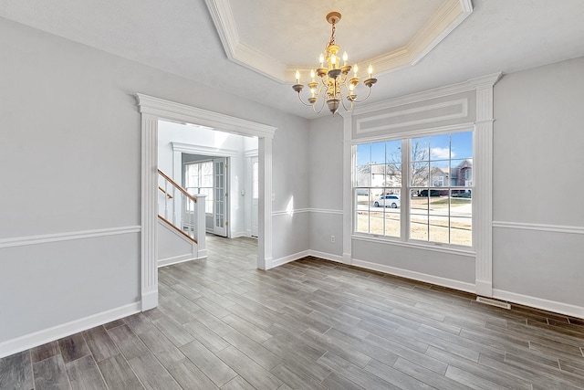 unfurnished dining area with a tray ceiling, a healthy amount of sunlight, dark wood finished floors, and an inviting chandelier