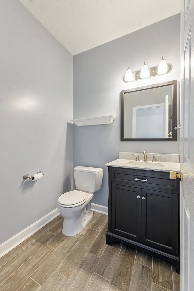 half bath featuring baseboards, vanity, toilet, and wood tiled floor