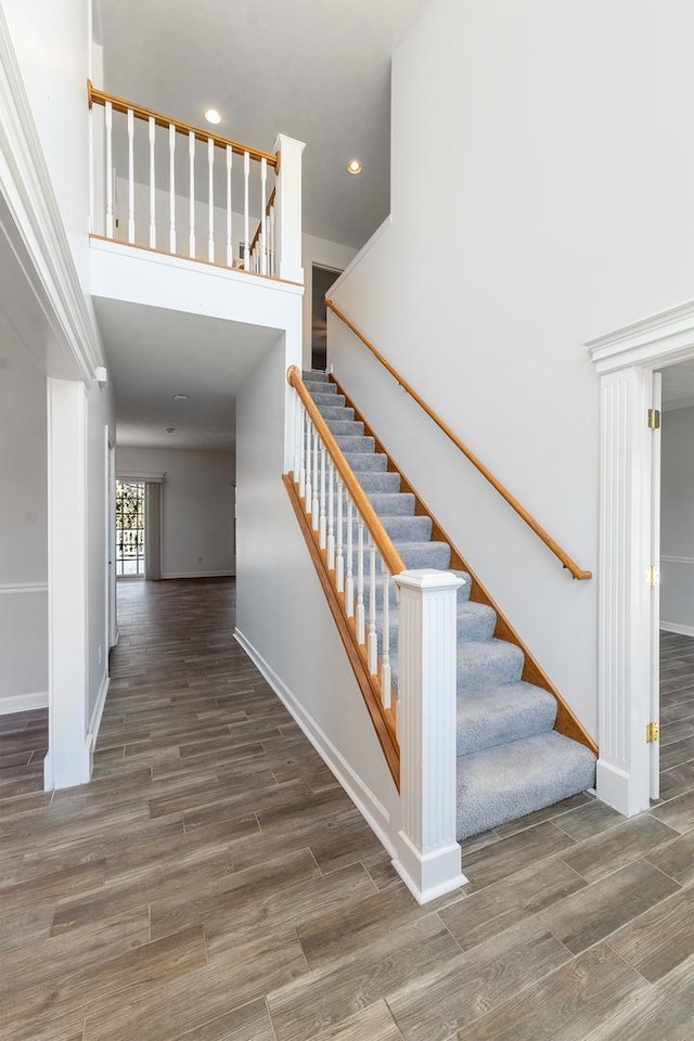 staircase with recessed lighting, a towering ceiling, baseboards, and wood finished floors