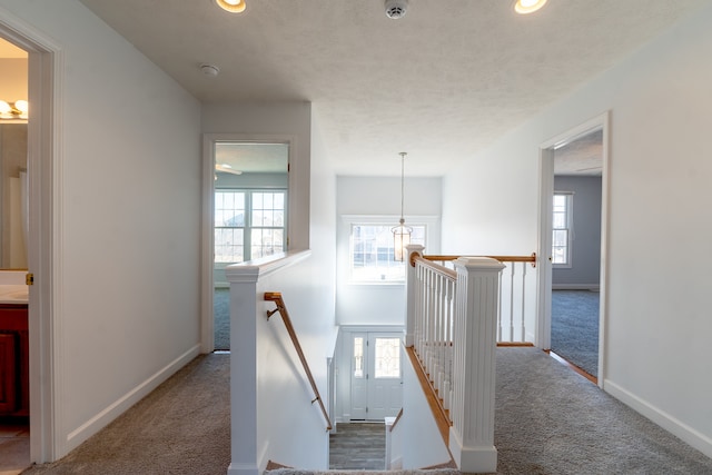 corridor featuring carpet floors, a wealth of natural light, baseboards, and an upstairs landing