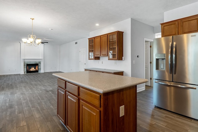 kitchen featuring stainless steel fridge, a kitchen island, brown cabinets, dark wood-type flooring, and a lit fireplace