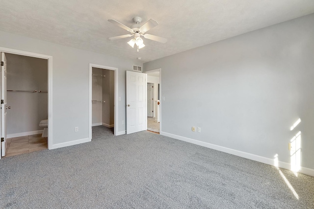 unfurnished bedroom with a textured ceiling, carpet floors, visible vents, baseboards, and a spacious closet