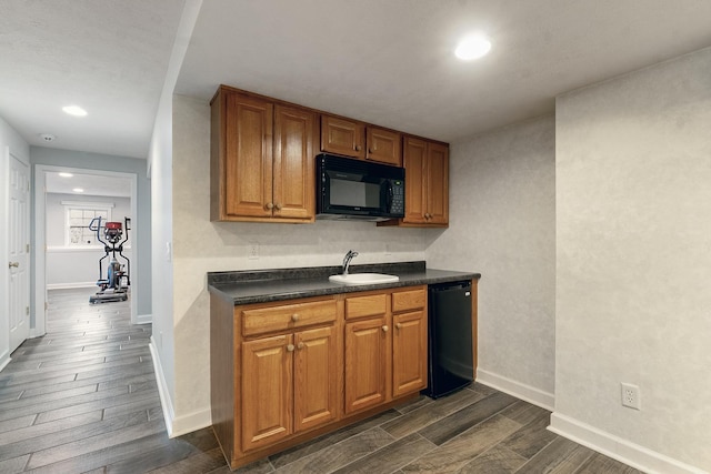 kitchen with a sink, wood tiled floor, black appliances, brown cabinetry, and dark countertops