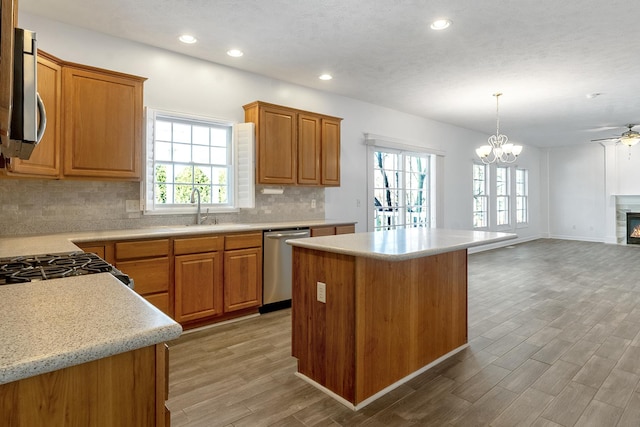 kitchen with light countertops, appliances with stainless steel finishes, backsplash, light wood finished floors, and a glass covered fireplace