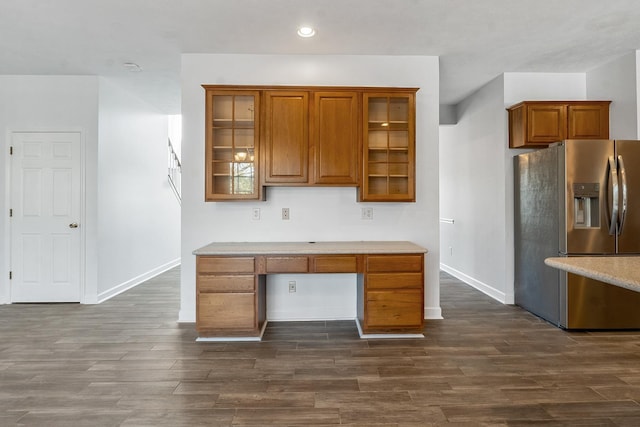 kitchen featuring brown cabinetry, built in desk, dark wood-type flooring, and stainless steel refrigerator with ice dispenser