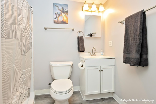 bathroom with toilet, wood finished floors, vanity, and baseboards