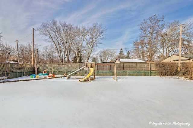 snow covered patio with a playground and a fenced backyard