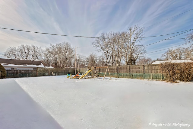 yard covered in snow featuring a playground and a fenced backyard