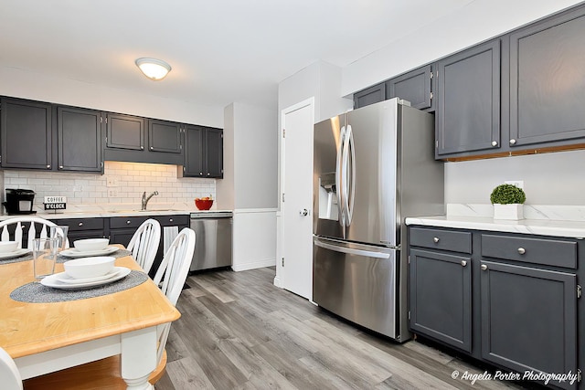 kitchen featuring tasteful backsplash, light wood-style flooring, gray cabinetry, appliances with stainless steel finishes, and a sink