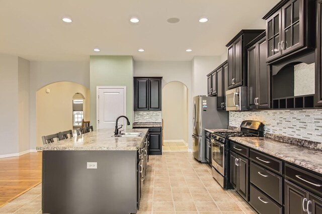 kitchen featuring a kitchen island with sink, a sink, recessed lighting, stainless steel appliances, and arched walkways