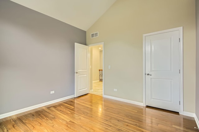 unfurnished bedroom with light wood-style flooring, visible vents, baseboards, and high vaulted ceiling