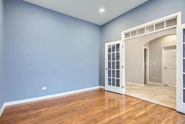 spare room featuring french doors, arched walkways, baseboards, and light wood-style flooring