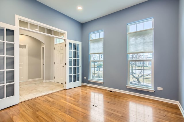 spare room featuring a wealth of natural light, french doors, arched walkways, and wood finished floors