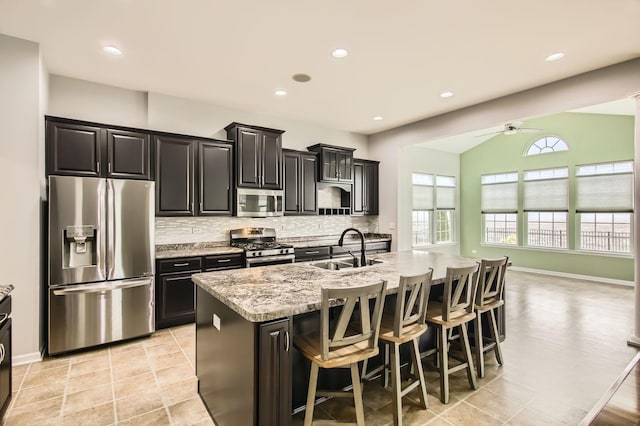 kitchen with a kitchen bar, an island with sink, a sink, appliances with stainless steel finishes, and decorative backsplash