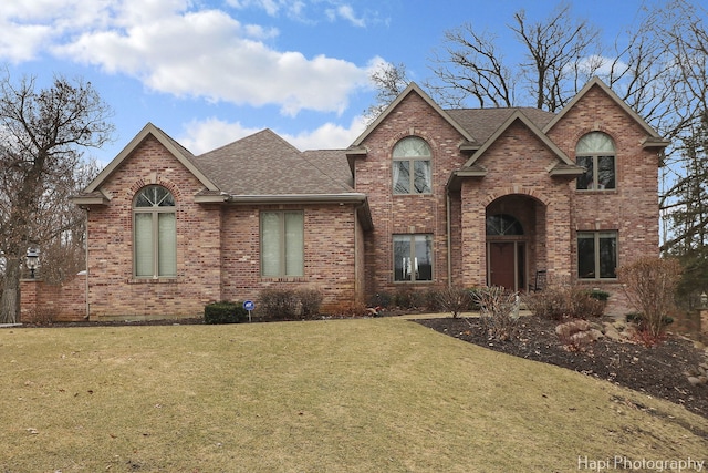 traditional-style house featuring a front yard, brick siding, and roof with shingles