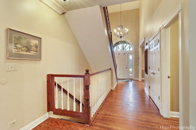 entrance foyer with an inviting chandelier, a towering ceiling, baseboards, and wood finished floors