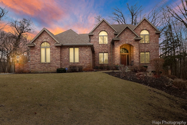 traditional-style home with a shingled roof, brick siding, and a yard