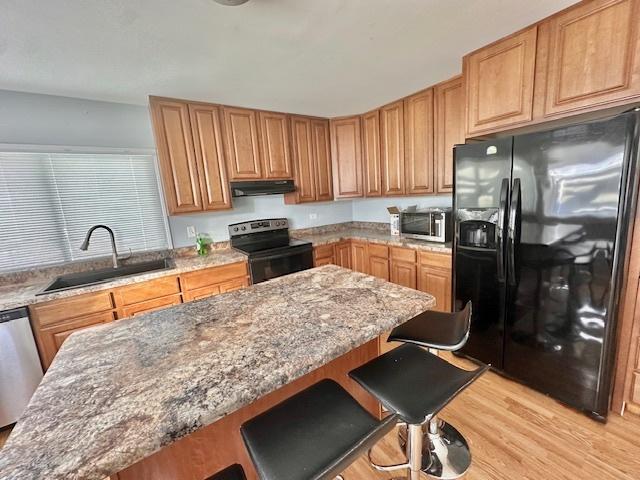 kitchen featuring light stone counters, under cabinet range hood, a sink, black appliances, and a kitchen bar