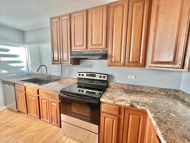 kitchen featuring brown cabinets, stainless steel appliances, light wood-type flooring, under cabinet range hood, and a sink