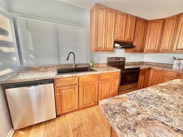 kitchen with light wood-style floors, light stone countertops, stainless steel appliances, under cabinet range hood, and a sink