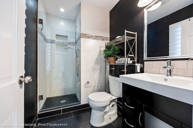 bathroom with toilet, vanity, tile walls, tile patterned floors, and a stall shower