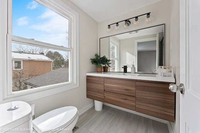 half bath with toilet, baseboards, and vanity