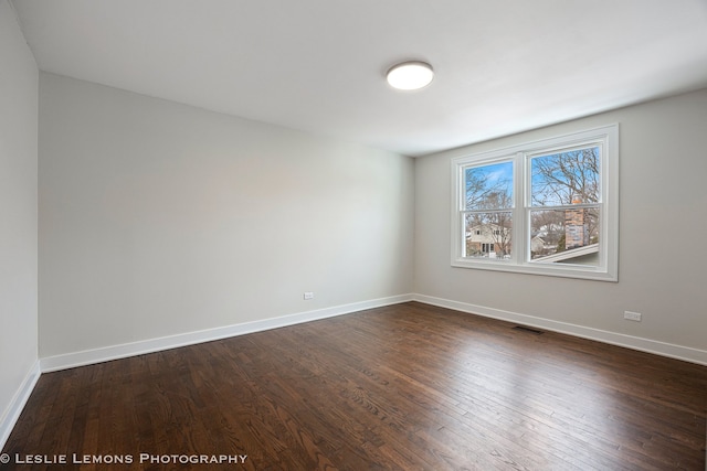 unfurnished room featuring dark wood-style floors, visible vents, and baseboards