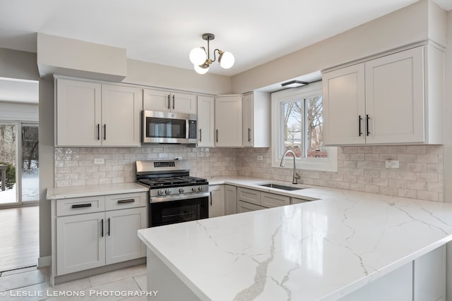 kitchen featuring a peninsula, appliances with stainless steel finishes, a sink, and light stone counters