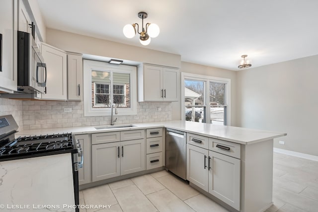 kitchen with light stone counters, appliances with stainless steel finishes, a peninsula, a sink, and backsplash