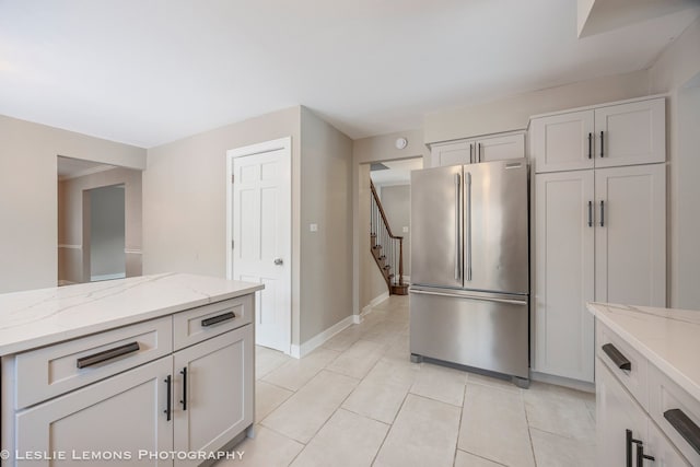 kitchen featuring light stone counters, freestanding refrigerator, baseboards, and light tile patterned floors