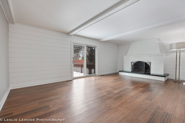 unfurnished living room with a brick fireplace, beam ceiling, baseboards, and wood finished floors