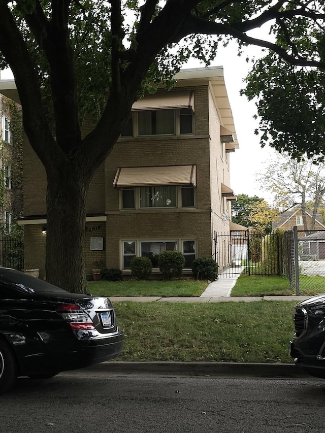 view of front of property featuring brick siding, fence, and a front lawn