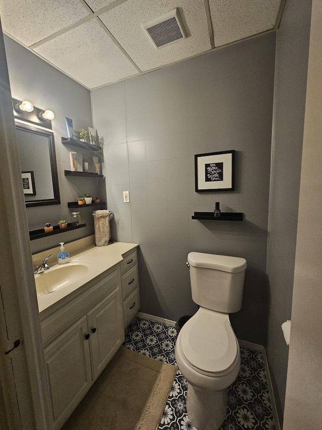 half bathroom with baseboards, visible vents, toilet, vanity, and a paneled ceiling