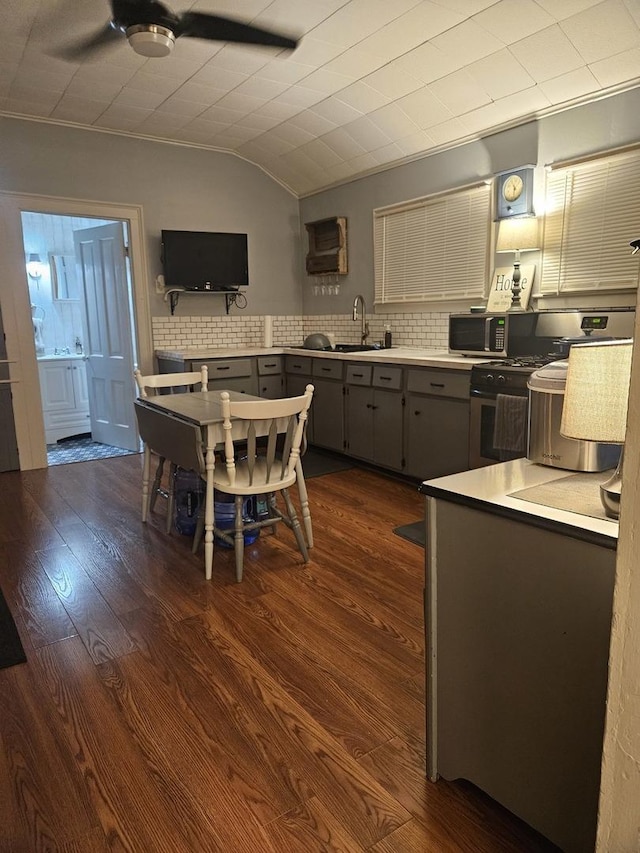 kitchen with a sink, gray cabinets, light countertops, and dark wood-style flooring