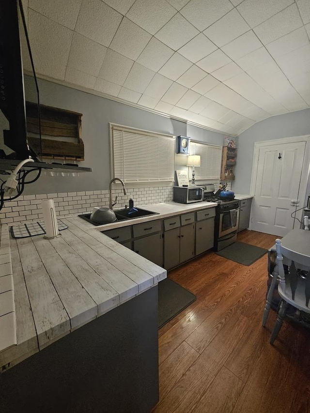 kitchen featuring stainless steel range with gas cooktop, gray cabinets, decorative backsplash, dark wood-type flooring, and a sink