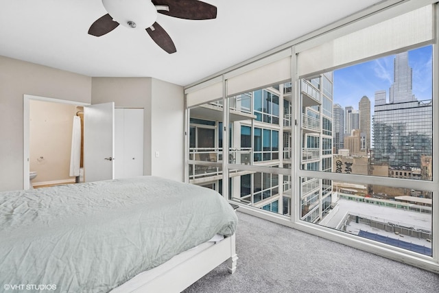 carpeted bedroom with a ceiling fan, a city view, and ensuite bathroom