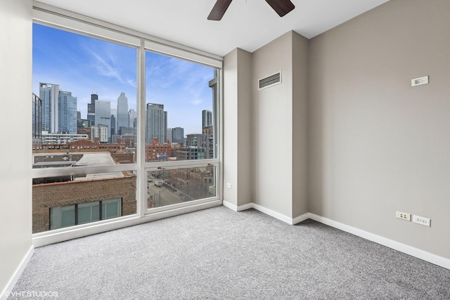 carpeted spare room with a wall of windows, visible vents, a city view, and baseboards