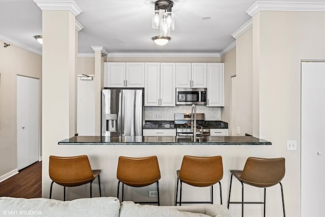 kitchen featuring a peninsula, appliances with stainless steel finishes, tasteful backsplash, a kitchen bar, and ornate columns