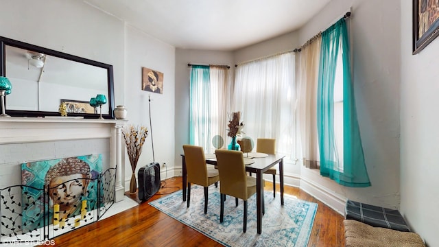 dining room with a brick fireplace, baseboards, and wood finished floors