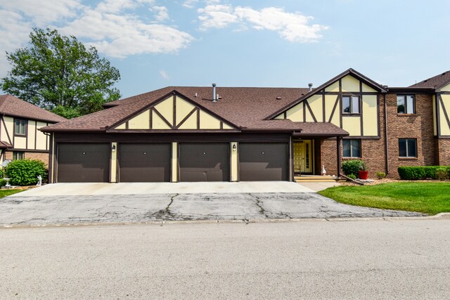 208 Carol Ct Unit A2, Pontiac, IL 61764 - tudor-style house featuring an attached garage, asphalt driveway, roof with shingles, and brick siding