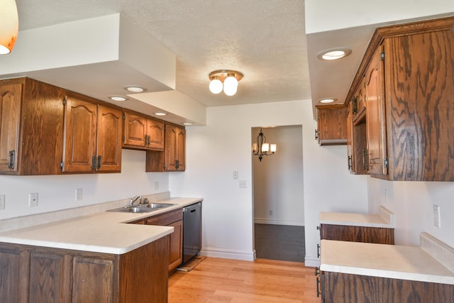 kitchen featuring a textured ceiling, a sink, light countertops, stainless steel dishwasher, and light wood finished floors