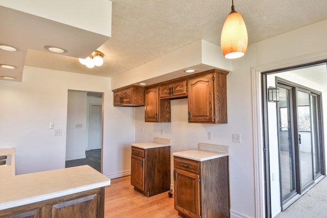 kitchen with a textured ceiling, baseboards, light wood-style floors, light countertops, and hanging light fixtures