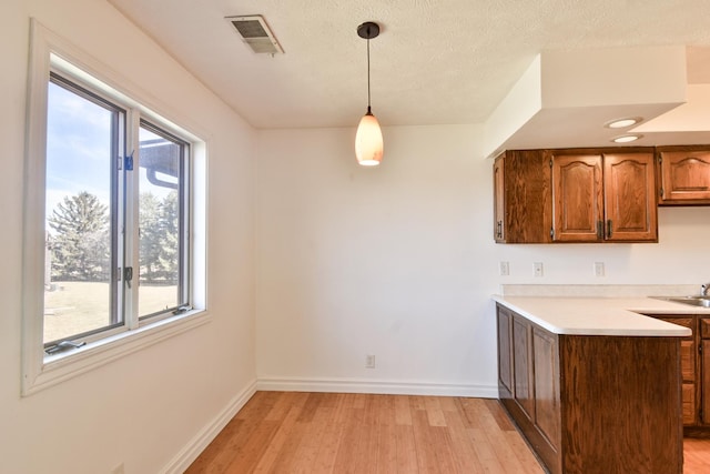 kitchen with a textured ceiling, light wood-style flooring, visible vents, baseboards, and light countertops