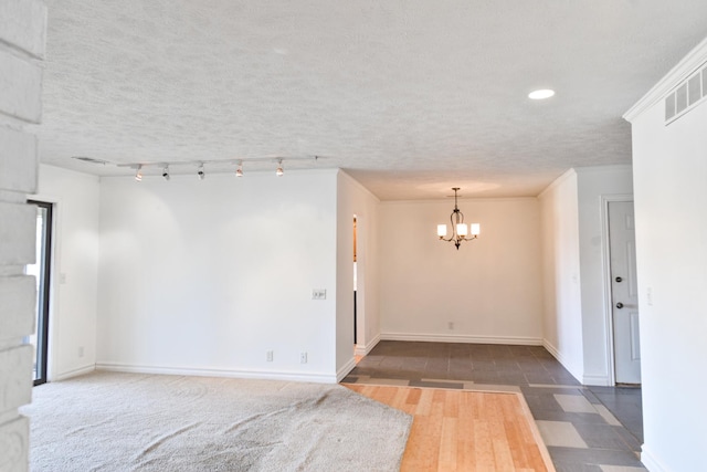 spare room with a textured ceiling, visible vents, baseboards, ornamental molding, and an inviting chandelier