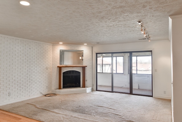 unfurnished living room with carpet floors, a brick fireplace, a textured ceiling, brick wall, and baseboards