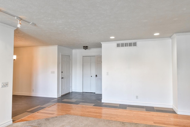 empty room featuring baseboards, visible vents, dark wood-style flooring, crown molding, and a textured ceiling