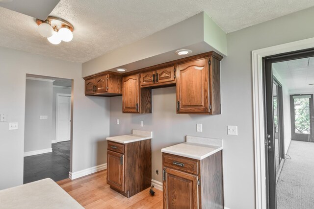 208 Carol Ct Unit A2, Pontiac, IL 61764 - kitchen with a textured ceiling, light wood-type flooring, baseboards, light countertops, and brown cabinetry